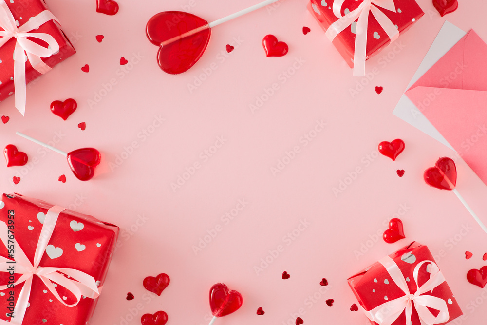 Love Valentines concept. Top view composition made of envelope with letter and red gift boxes, heart lollipops with sprinkles on pastel pink background with copy space in the middle. Love Valentines concept. Top view composition made of envelope with letter and red gift boxes, heart lollipops with sprinkles on pastel pink background with copy space in the middle.