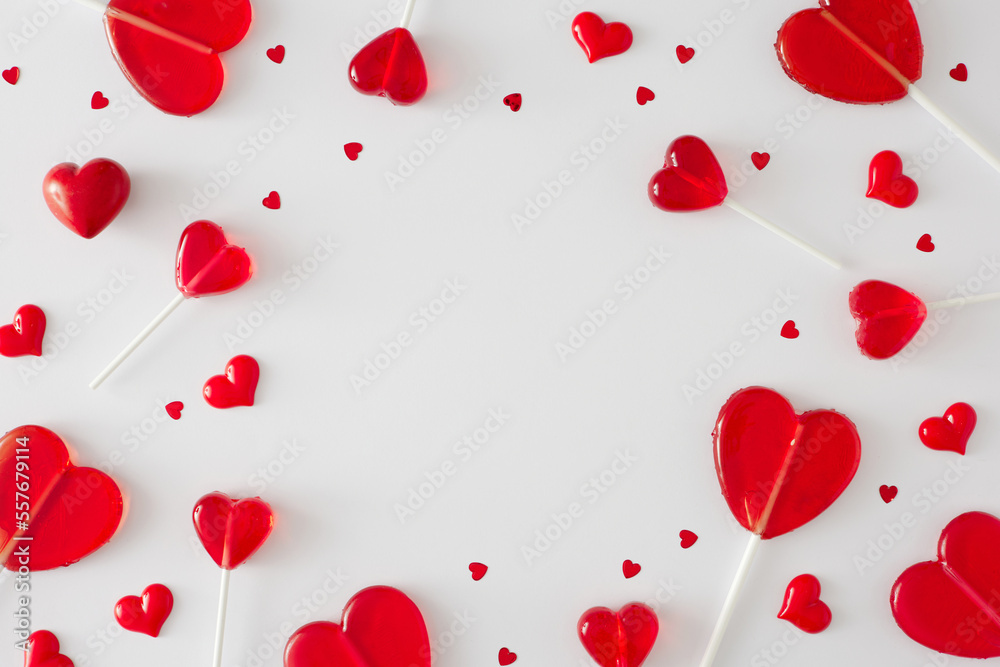 Valentine's Day concept. Flat lay photo of red heart shaped lollipops and sprinkles on white background with copy space in the middle. Sweet Valentines card idea.