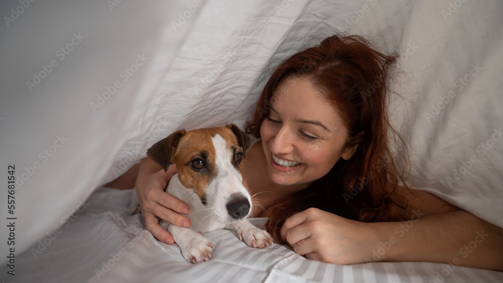 Caucasian red-haired woman sleeps in an embrace with a jack russell terrier dog on a white sheet. Caucasian red-haired woman sleeps in an embrace with a jack russell terrier dog on a white sheet.