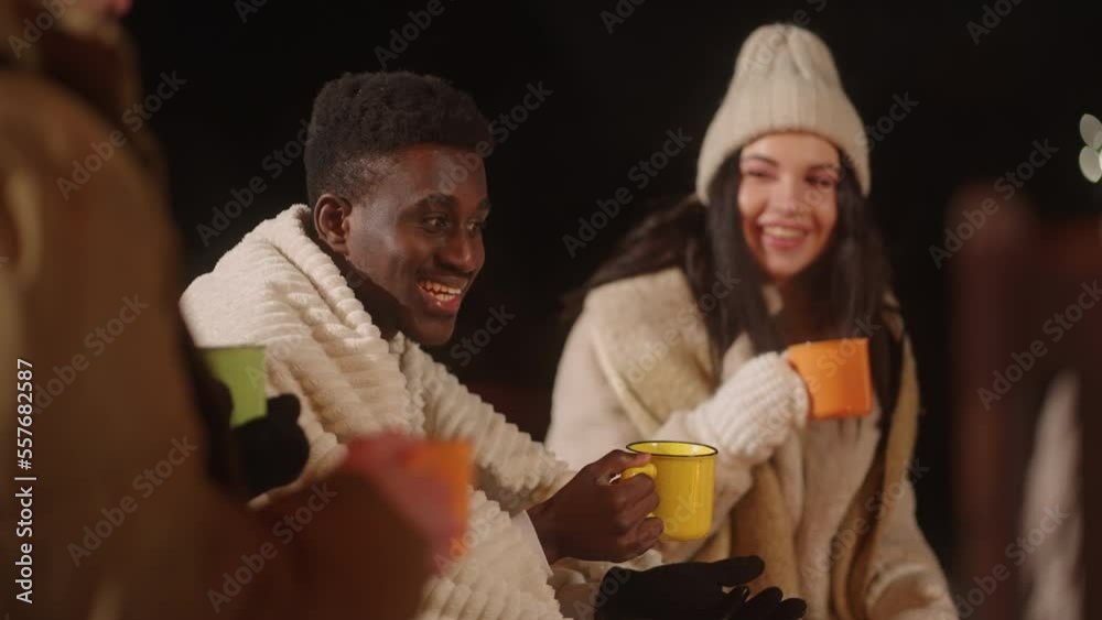 black guy and his caucasian friends have fun together, warming near campfire in winter night