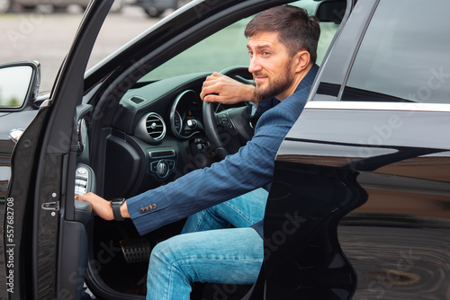 Successful business man with a phone in his hand sits behind the wheel of a prestigious car © photosaint
