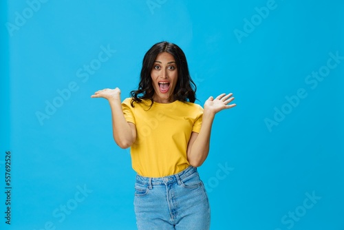 Woman in yellow t-shirt on blue background posing gestures emotions and signals with smile, hands up happiness copy space