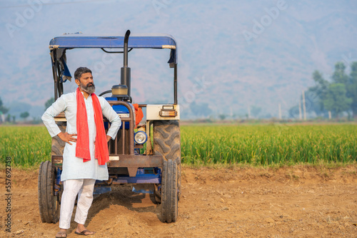 Indian farmer standing near tractor and giving expression at agriculture field.