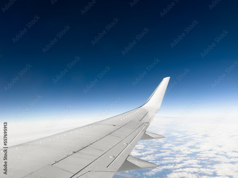 White wing from airplane window on sunny day. Great views of landscape. Aerial view of clouds through a plane window. Wing of airplane with blue sky and beauty clouds