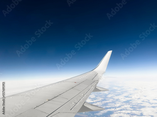 White wing from airplane window on sunny day. Great views of landscape. Aerial view of clouds through a plane window. Wing of airplane with blue sky and beauty clouds