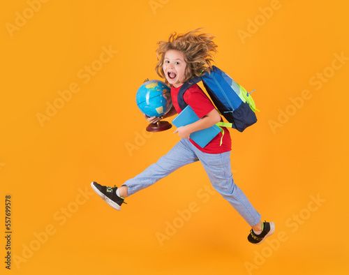 Shool kid jump with school bag and globe. Full length body of little school kid jumping having fun isolated yellow color background. Crazy school boy jump.