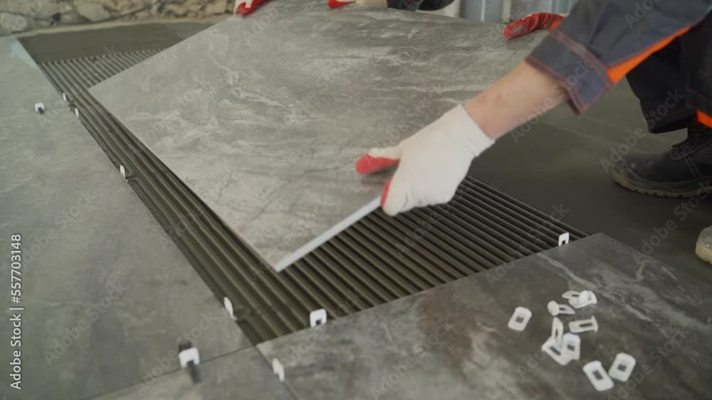 Workers are laying the floor with large tiles. A worker puts a large tile on the floor. Workers are installing a large ceramic tile on the floor.