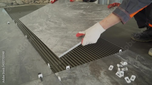 Workers are laying the floor with large tiles. A worker puts a large tile on the floor. Workers are installing a large ceramic tile on the floor.