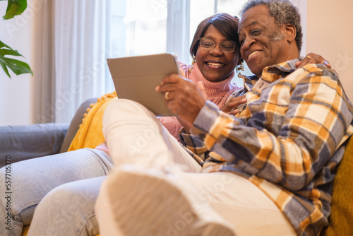 Senior couple using the tablet on the sofa in their living room and having a quality fun time