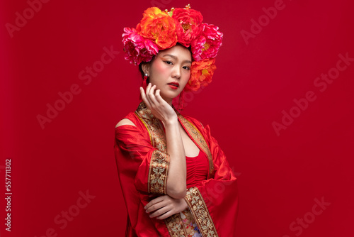 Portrait of young asian woman wearing fashion modern qipao cheongsam dress smile and flower on head on red background for Chinese new year festival photo
