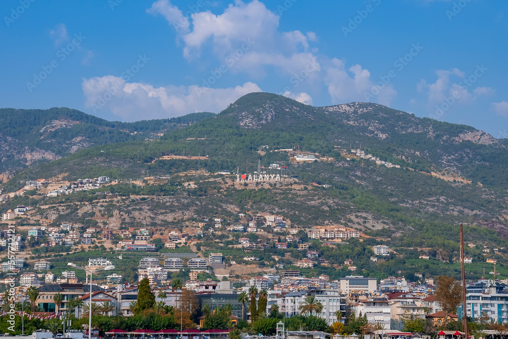 Side, Turkey. October 10, 2022. Low angle distant view of Alanya text with heart shape on majestic mountain in city with blue sky in the background during sunny day