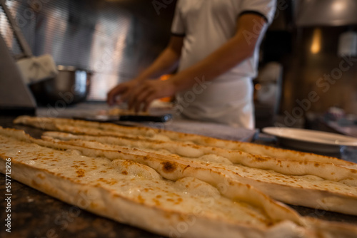 Close-up of fresh Turkish cheese pide on kitchen counter and midsection of male chef cooking in the background at restaurant