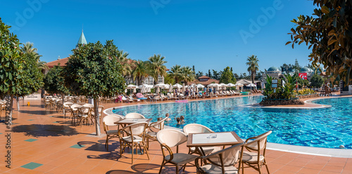 Tables and chairs arranged around swimming pool with clear blue sky in the background at tourist resort during sunny day at Side, Turkey