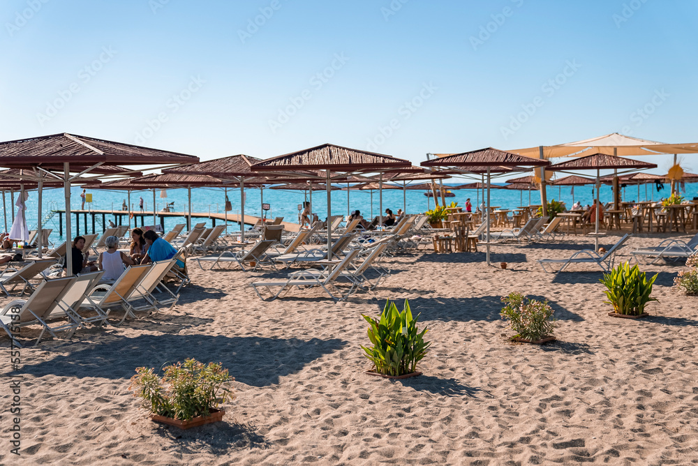 Side, Turkey. October 10, 2022. Deckchairs with wooden parasols and plants arranged on sandy beach with clear blue sky in the background during sunny day