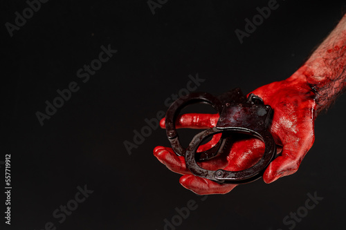 Fototapeta Naklejka Na Ścianę i Meble -  Faceless man holding handcuffs black background. Hands are stained with blood.
