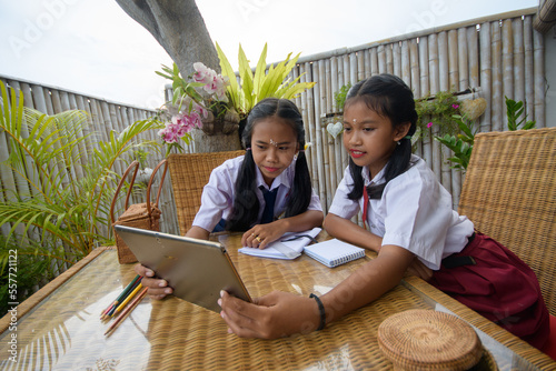 Two girls children girls with ponytails are learning and sitting at the table in school uniform, Indonesia