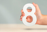 Eight in hand. A hand holds a white number 8 on a blurred background. Concept with number eight. Birthday 8 years, percentage, eighth grade or day, international women's day.