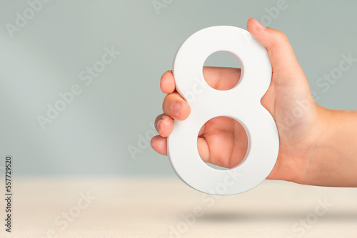 Eight in hand. A hand holds a white number 8 on a blurred background. Concept with number eight. Birthday 8 years, percentage, eighth grade or day, international women's day. photo