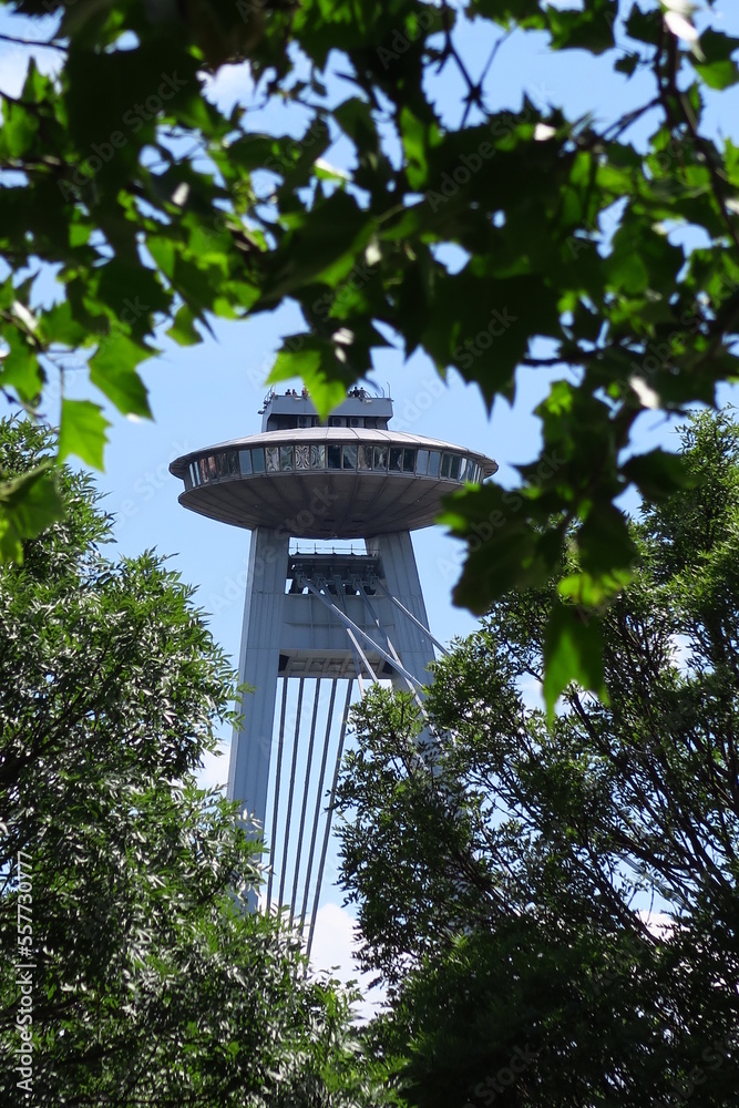 famous bridge novy most with ufo saucer building on the top in Bratislava viewed through green trees and blue sky in summer in slovakia famous bridge novy most with ufo saucer building on the top in Bratislava viewed through green trees and blue sky in summer in slovakia
