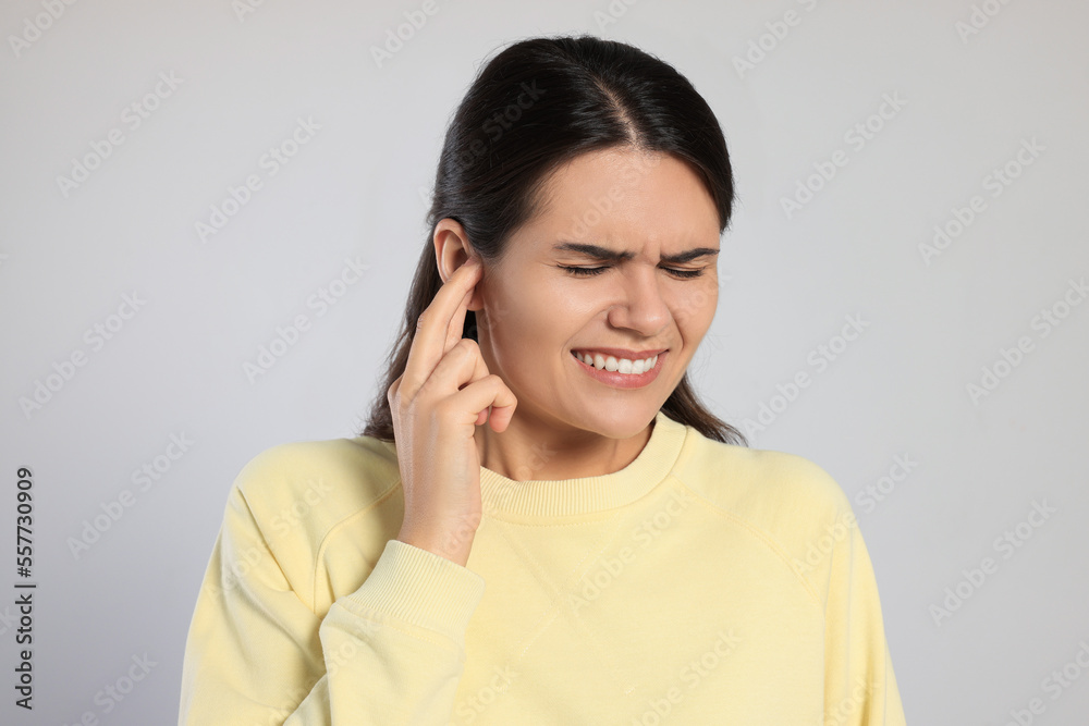 Young woman suffering from ear pain on light grey background Young woman suffering from ear pain on light grey background