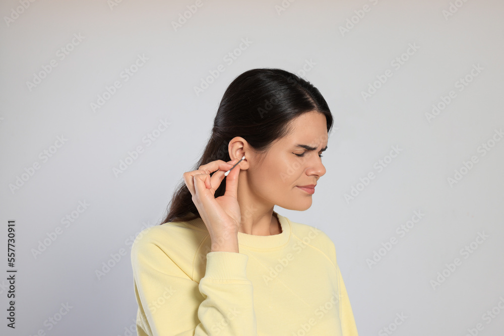 Young woman cleaning ear with cotton swab on light grey background Young woman cleaning ear with cotton swab on light grey background
