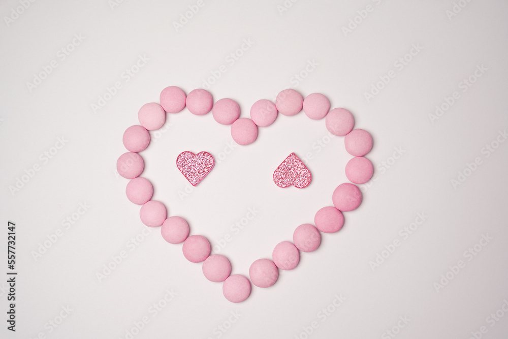  Sweets candies as heart with two glittering pink hearts on white background. Valentines day concept. Flat lay.