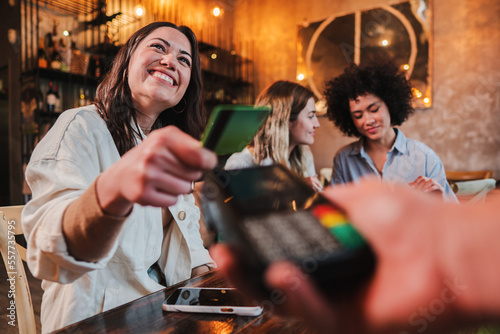 Happy young woman paying bill with a contactless credit card in a restaurant. Female smiling holding a creditcard and giving a payment transaction to the cashier. High quality photo photo
