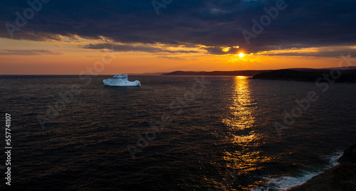 Newfoundland iceberg golden sunset landscape scene with streaming sunset light reflections in water, outdoor evening ocean view.