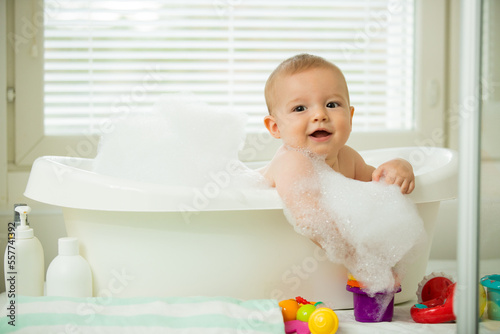 Tableau sur toile Cute little baby sitting in white bathtub with foam and soap bubbles