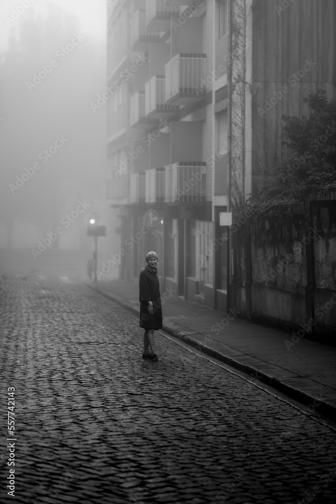 A woman enjoys the atmosphere on a deserted street in the thick fall morning fog. Black and white photo.
