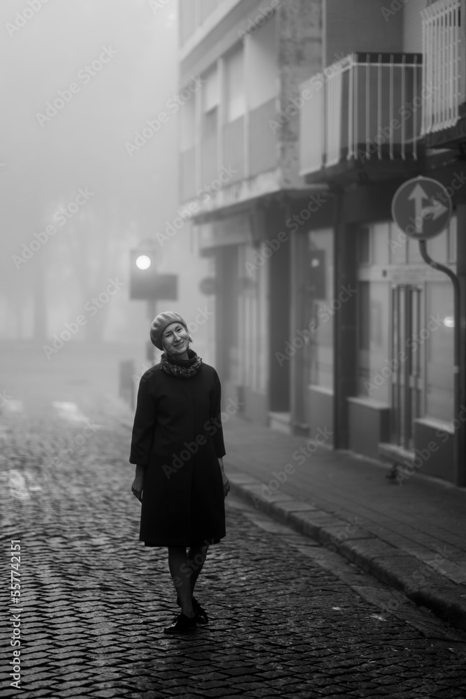 A woman enjoys the atmosphere on the sidewalk in the thick fall morning fog.