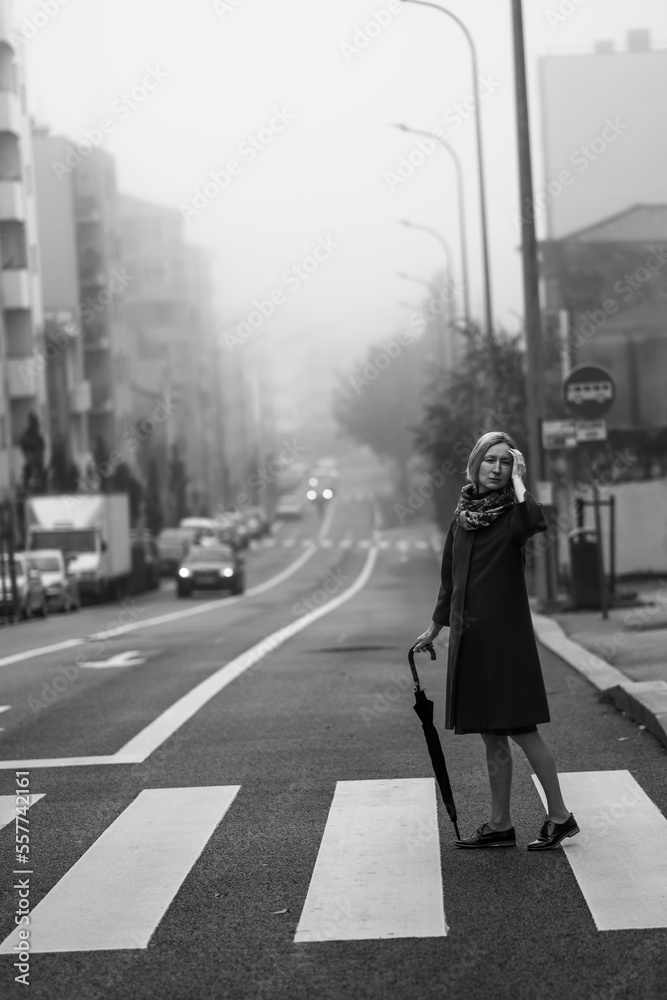 A woman with an umbrella stands outside in the fog. Black and white photo.