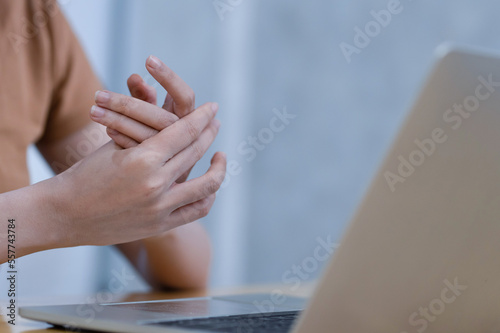 Closeup woman holding her hand pain from using laptop computer long time. Office syndrome concept. Young woman working in office with a carpal tunnel syndrome or wrist joint inflammation.
