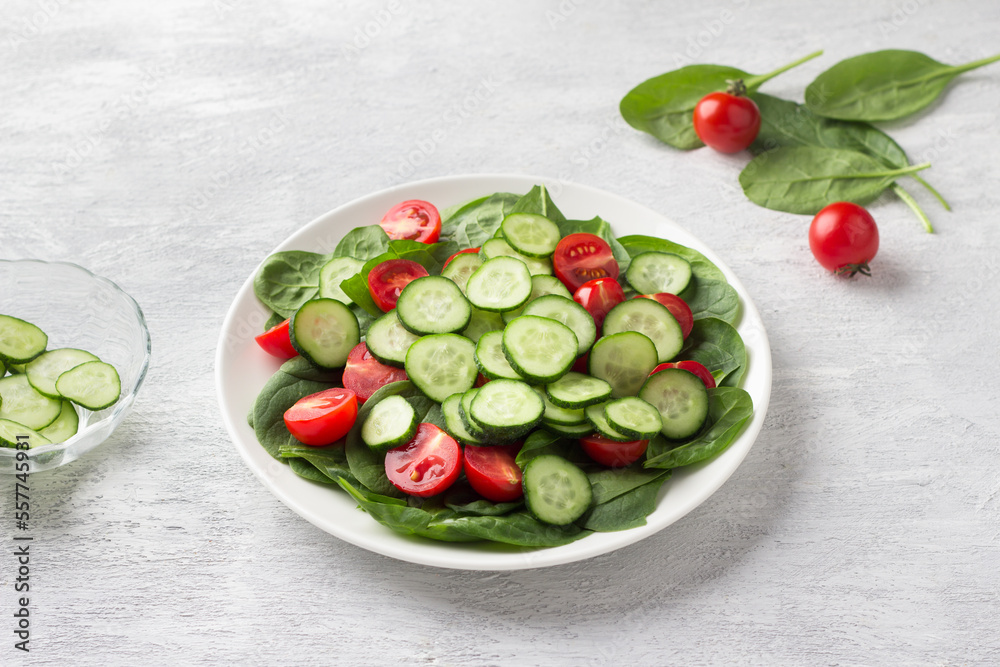 Plate with fresh spinach leaves, cucumbers and cherry tomatoes on a light gray background. delicious healthy food