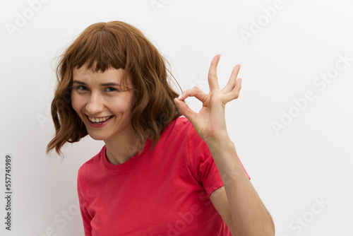 a happy, joyful woman poses standing on a white background in a pink T-shirt and smiling pleasantly shows the ok sign
