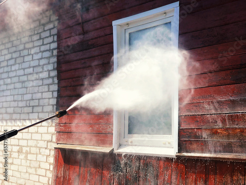 Foto High pressure spray gun washing the white window and red wall of a wooden villag