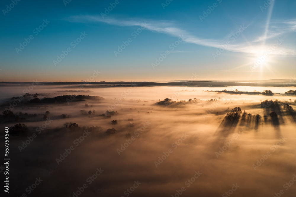 Flying over a village at dawn, bright sun on the horizon and fog over a small village.