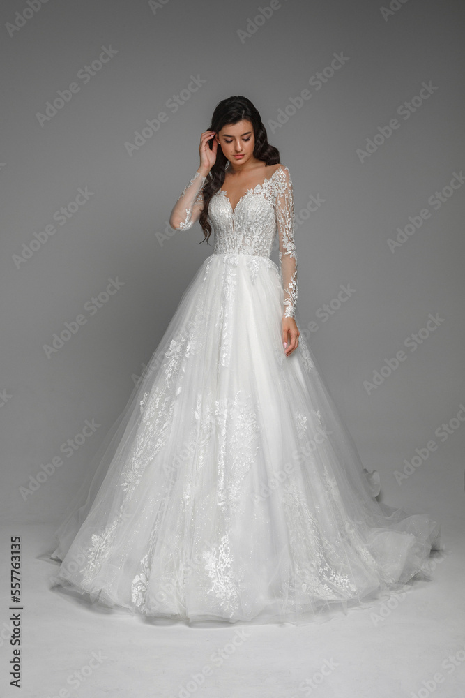Full length bride portrait. Elegant woman in white wedding dress standing in grey interior.Attractive female model standing and posing in ball gown.