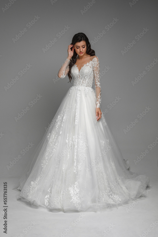Full length bride portrait. Elegant woman in white wedding dress standing in grey interior.Attractive female model standing and posing in ball gown. Full length bride portrait. Elegant woman in white wedding dress standing in grey interior.Attractive female model standing and posing in ball gown.