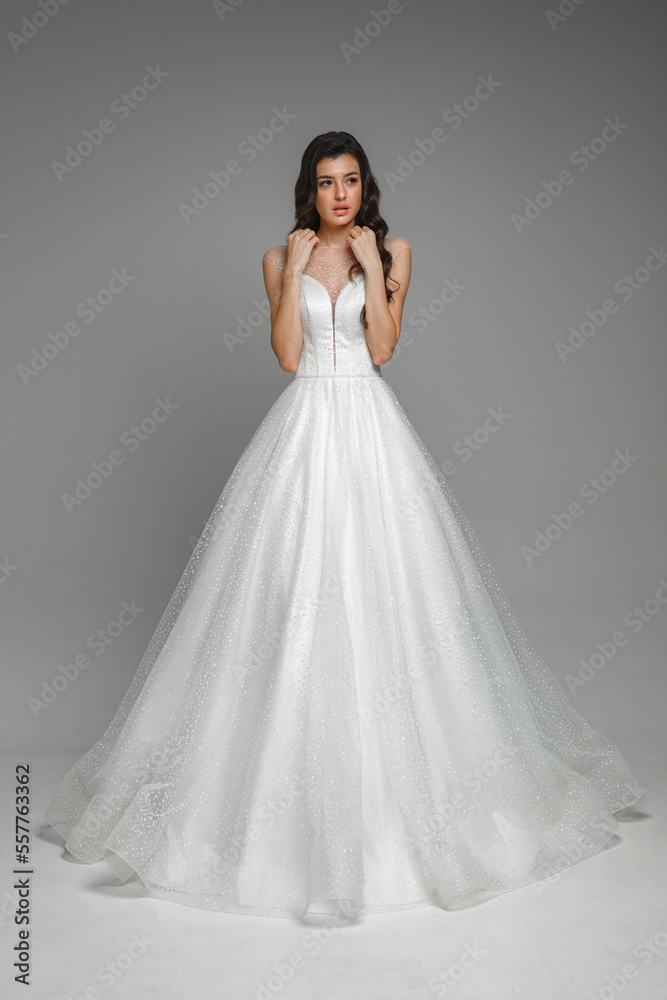 Full length portrait of young beautiful woman wearing white wedding dress. Elegant bride standing and posing with hands in the studio.Gorgeous female on a grey isolated background. Full length portrait of young beautiful woman wearing white wedding dress. Elegant bride standing and posing with hands in the studio.Gorgeous female on a grey isolated background.