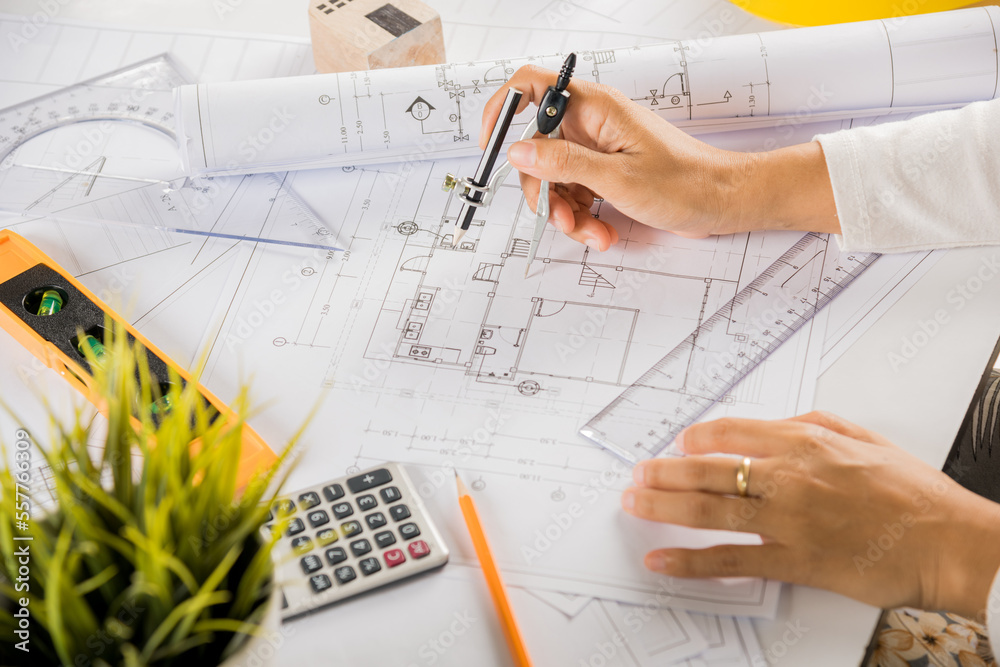 Architectural project workplace. Architect drawing with divider compass on house plan blueprint paper for repair tools on table desk at architecture office, Engineer sketching construction project Architectural project workplace. Architect drawing with divider compass on house plan blueprint paper for repair tools on table desk at architecture office, Engineer sketching construction project