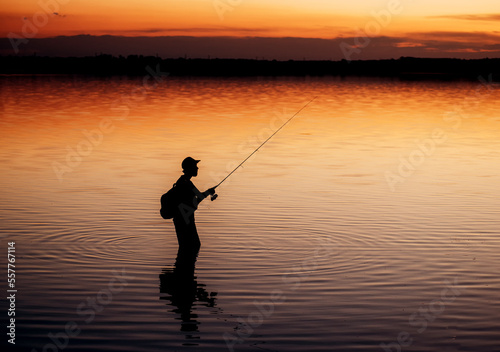 A fisherman silhouette fishing with spinning at sunset. Freshwater fishing, catch of fish