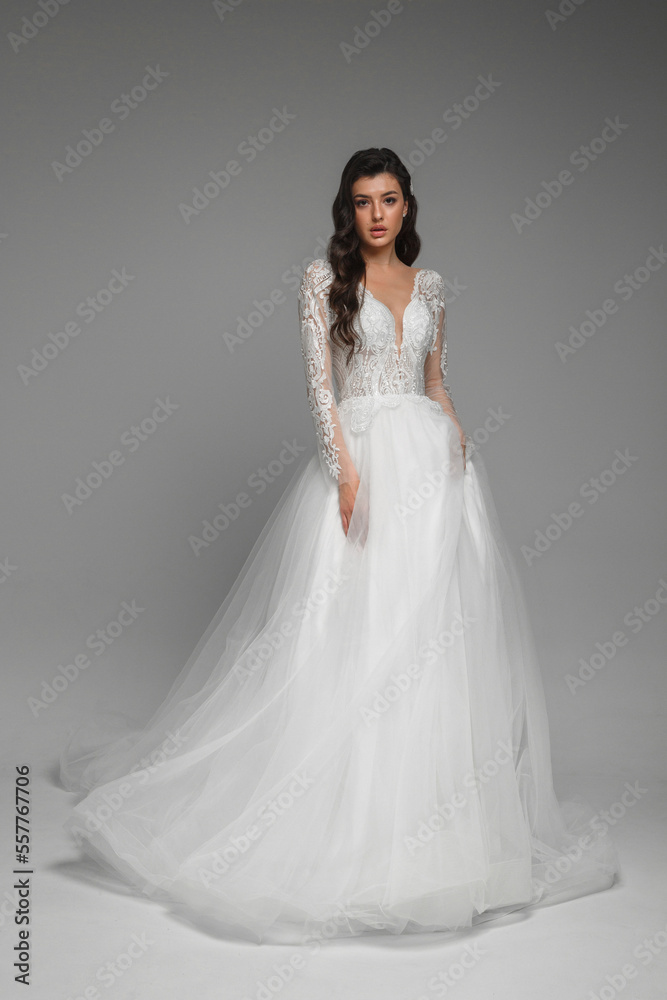 Portrait of the full lengthelegant woman wearing beautiful white wedding dress with embroidery on the sleeves. Attractive bride standing and posing.