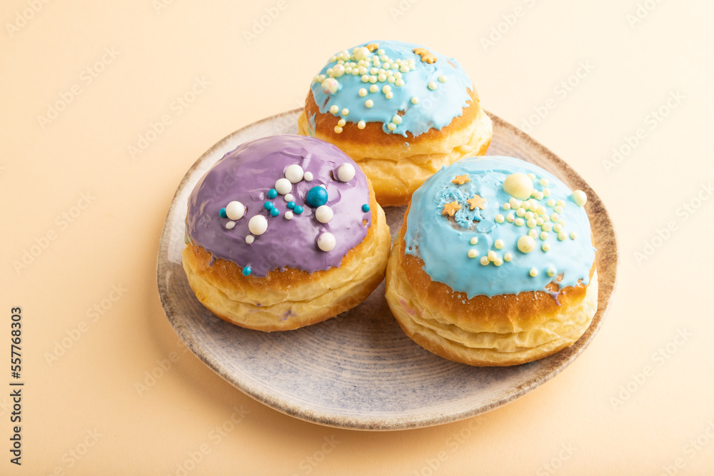 Purple and blue glazed donut on orange pastel, side view.