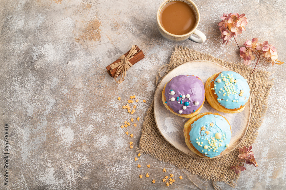 Fototapeta premium Purple and blue glazed donut and cup of coffee on brown concrete, top view, copy space.