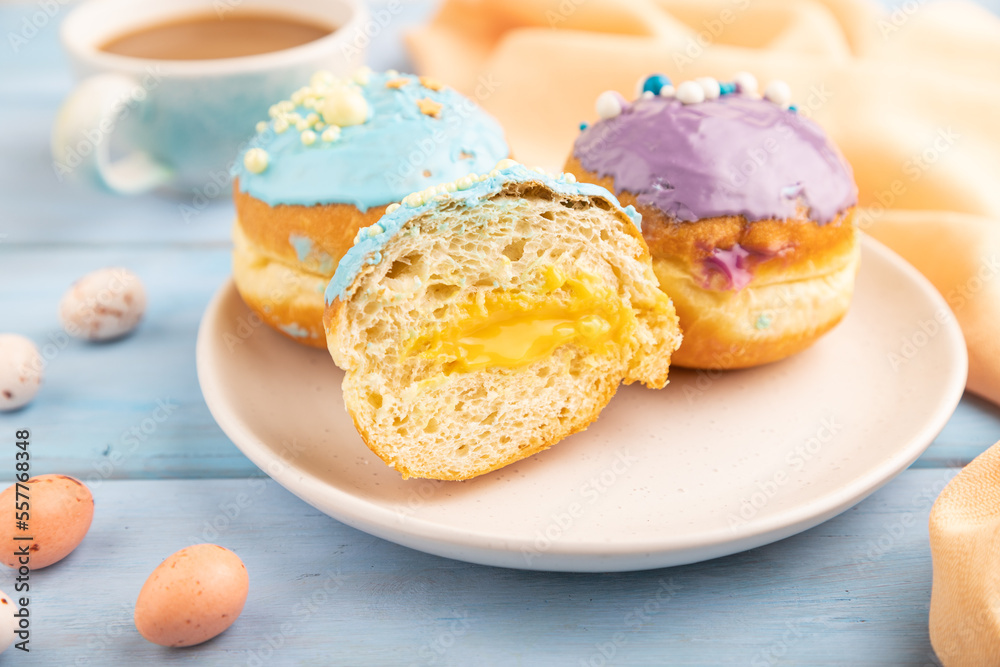 Purple and blue glazed donut and cup of coffee on blue wooden, side view, selective focus. Purple and blue glazed donut and cup of coffee on blue wooden, side view, selective focus.