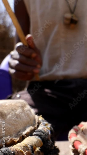 Vertical video of Close shot of black man playing dundun with wooden sticks while sitting photo