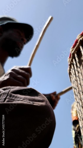 Vertical video of Wide shot of black man playing dundun with wooden sticks while sitting photo