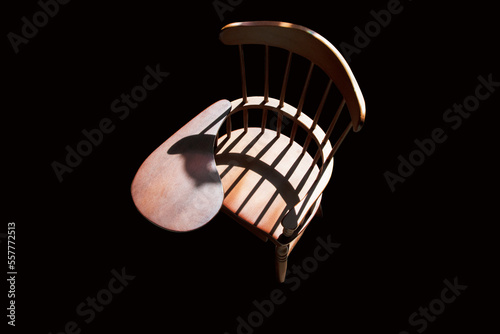 Old style wooden school desk chair contrast against dark background with shadows from rear daylight source, indoor.