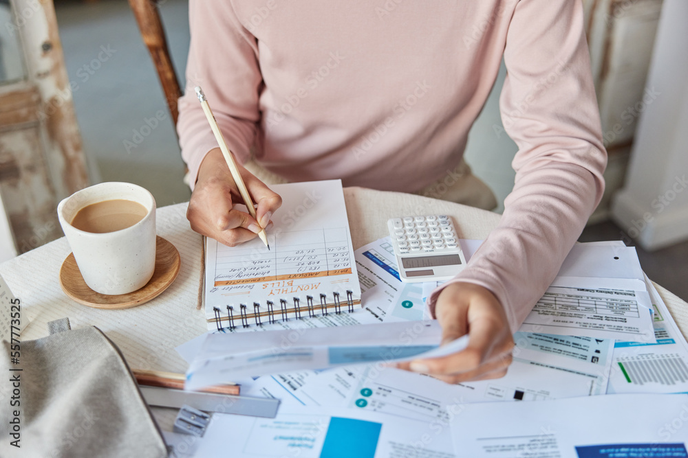 Cropped shot of unknown woman poses at home office makes calculations of utility payments writes down notes in spiral notebook surrounded by paper bills and cup of coffee calculates domestic expenses - obrazy, fototapety, plakaty 